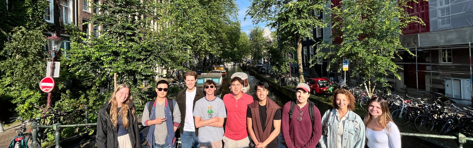 Students posing on a bridge over a canal with boats in the distance. 